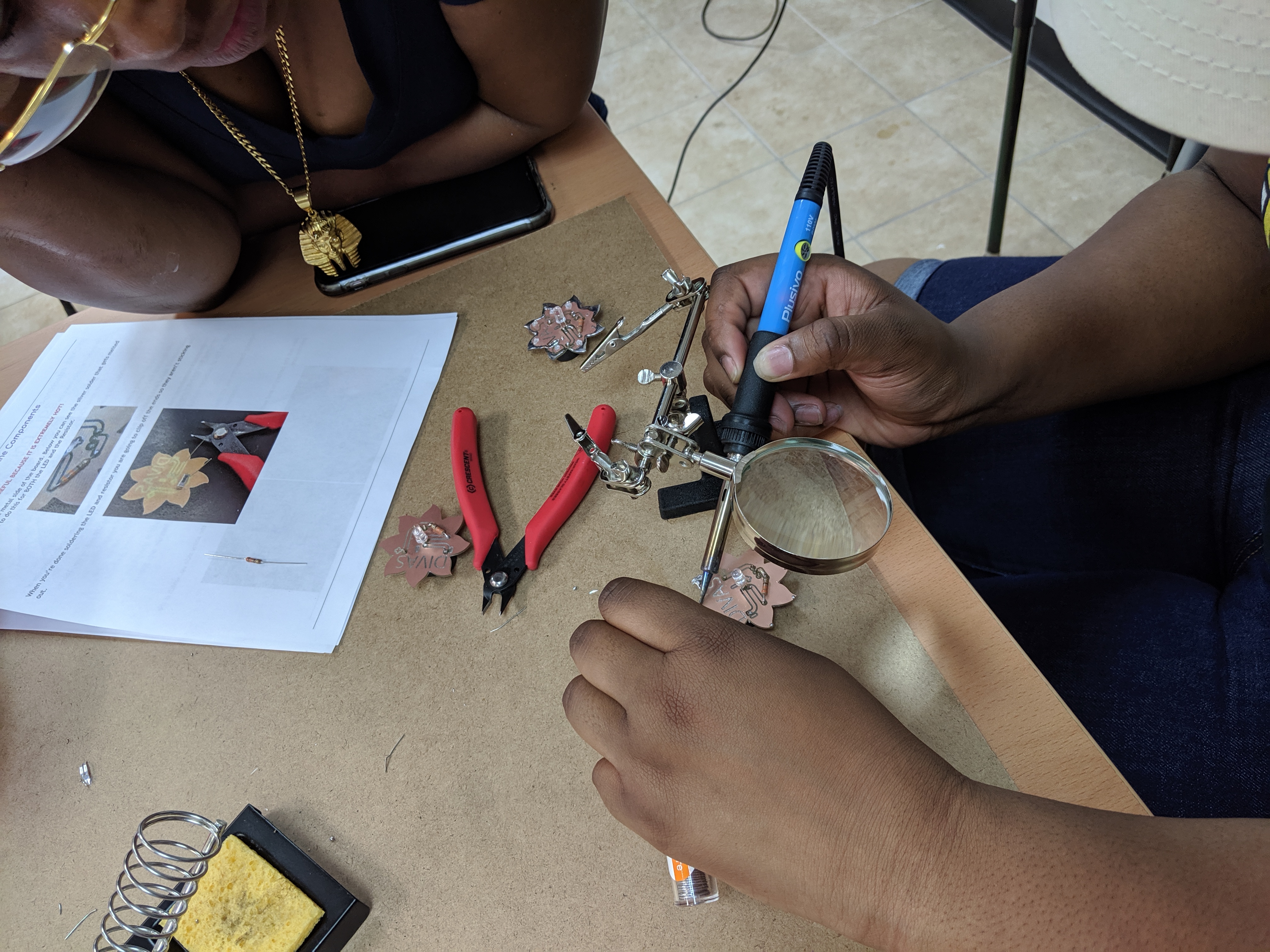 person soldering an LED circuit board with the DIVAs logo